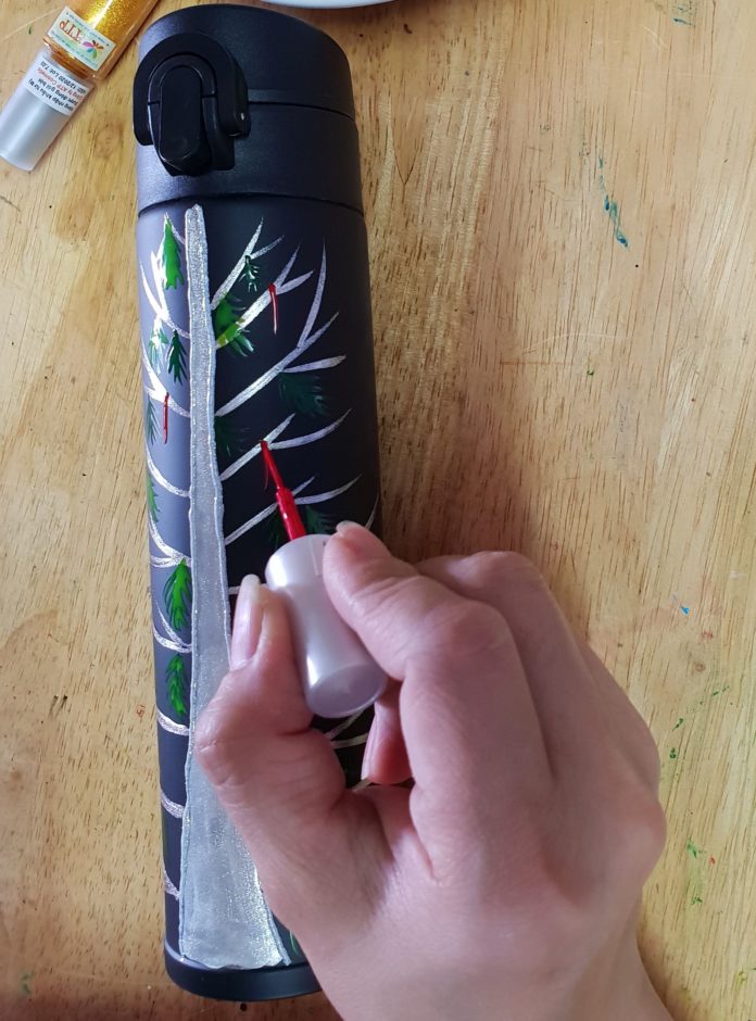 Tiến hành vẽ dải nơ đỏ buộc quà cho cây thông. (Nguồn BlogAnChoi)