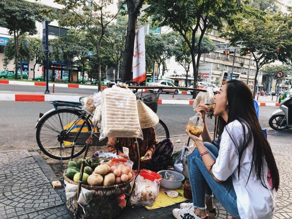 Kim Duyên ngồi ăn bánh tráng trộn ở gánh hàng rong lề đường (Ảnh: FB Nguyễn Huỳnh Kim Duyên)