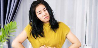 Asian woman suffering from stomachache, GERD after eating spicy food hand holding her pain stomach sitting at the table
