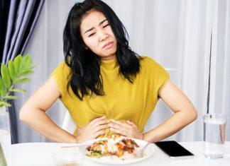 Asian woman suffering from stomachache, GERD after eating spicy food hand holding her pain stomach sitting at the table