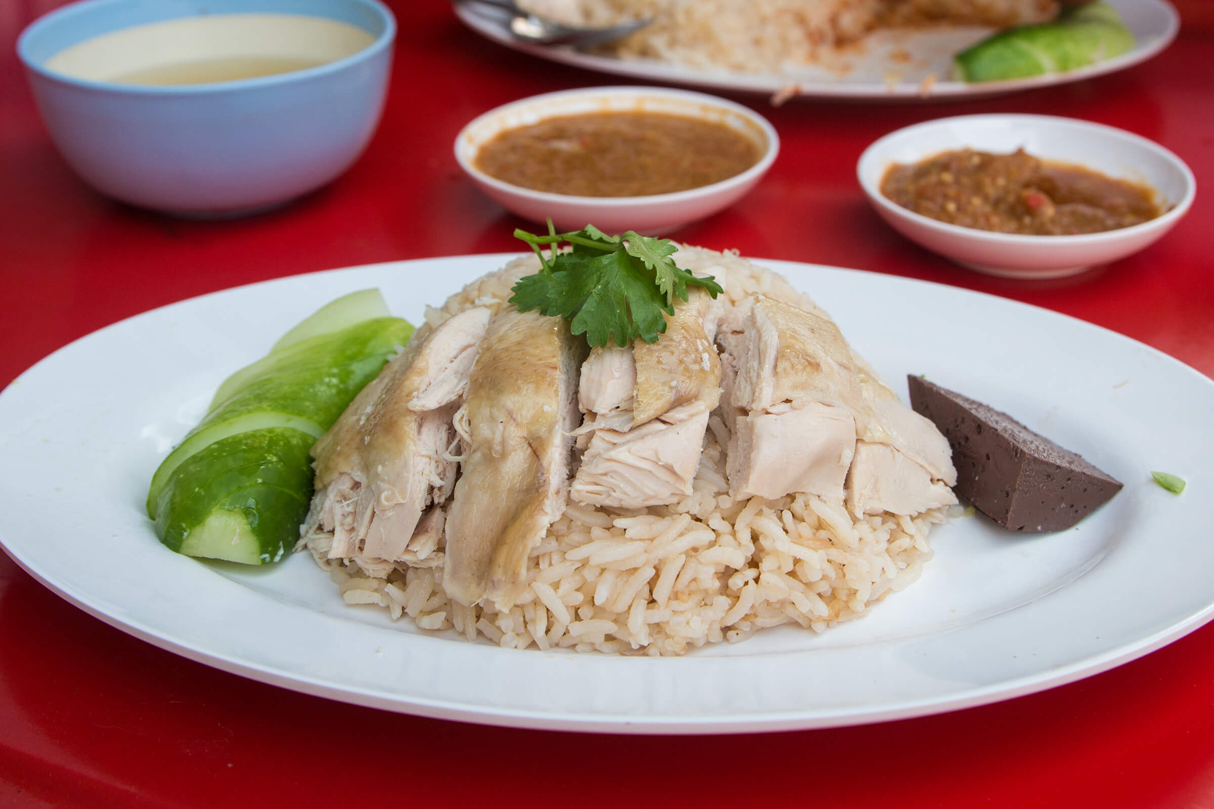 Khao Man Gai thường được ăn bằng tay. Thực khách sẽ xé nhỏ gà thành từng miếng, sau đó chấm vào nước sốt và ăn kèm với cơm. Dưa leo, cà chua và gừng chua cũng được ăn kèm để tăng thêm hương vị cho món ăn.